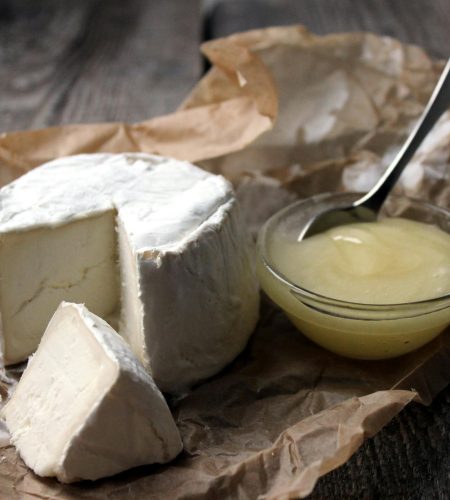 Close-up of gourmet soft cheese with a portion cut out, served with honey on rustic brown paper.